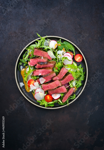 Modern style traditional fried dry aged bison beef rump steak slices with vegetable, lettuce and mustard dressing served as top view on a Nordic design plate with copy space