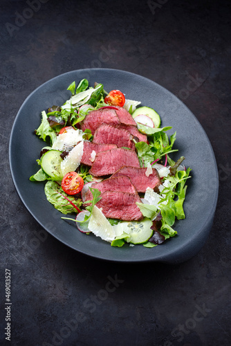 Modern style traditional fried dry aged bison beef rump steak slices with vegetable, lettuce and parmesan cheese served as top view on a design plate with copy space
