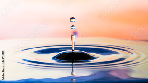 Drops of water falling on the water surface cause ripples and reflections on a orange sunset gradient background.