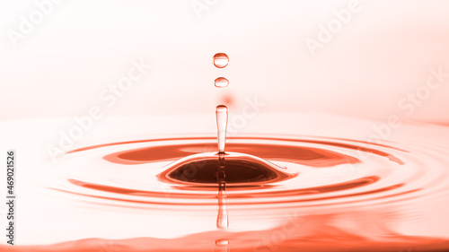 Abstract droplets of water on water surface to create ripples with orange-pink background.