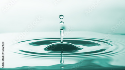 Water drop falling on water surface created ripples on blue green shadow light background.