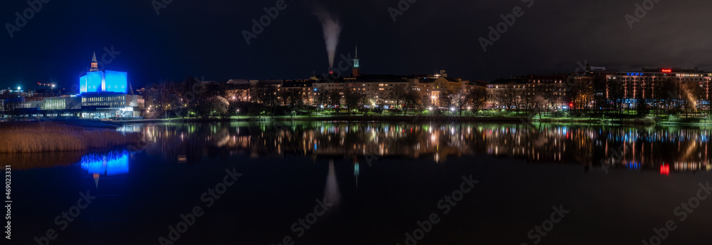 Fototapeta premium Beautiful city skyline casting reflections on the calm water during the night.
