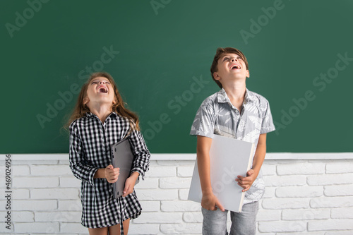 School children hold book with surprising expression against blackboard. School kids friends.