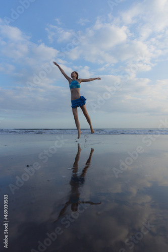 Slim Caucasian woman jumping on the beach. Active lifestyle. Fit and healthy. Happiness and freedom. Young female wearing blue bikini. Water reflection. Sunset time. Copy space. Bali © Olga
