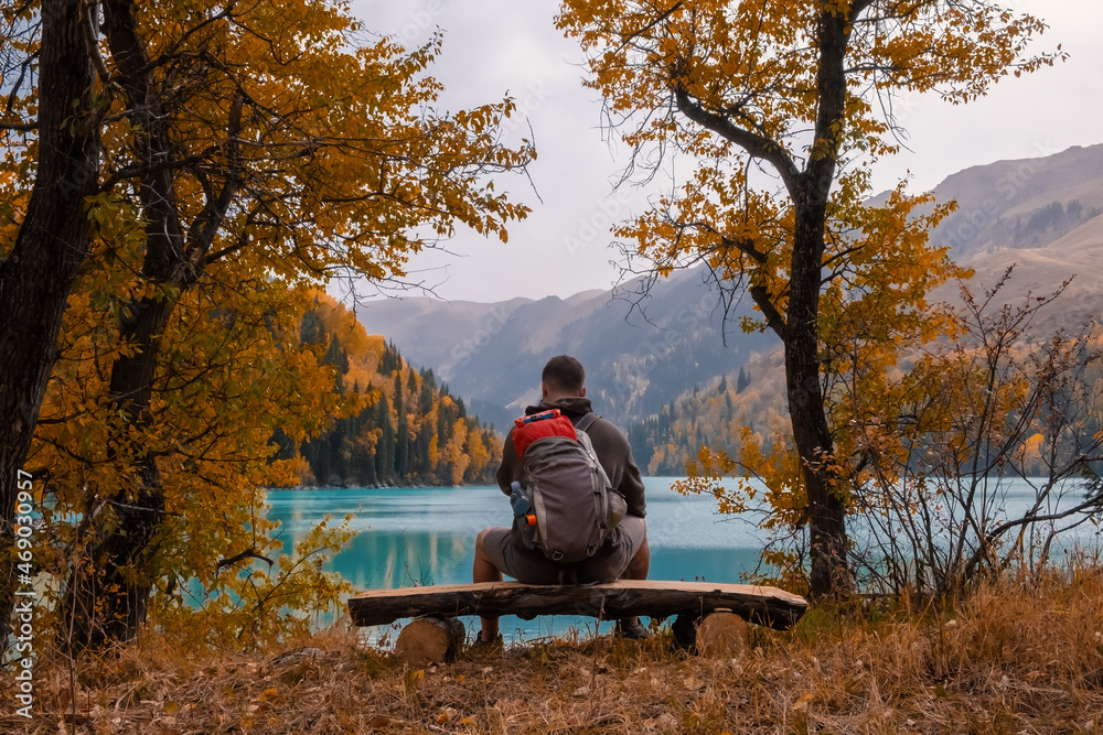 Tourist is resting on the bench near beautiful mountains lake with turquoise water and colorful forest. Tourism, trekking, hiking in autumn concept. Tourist is resting on the bench near beautiful mountains lake with turquoise water and colorful forest. Tourism, trekking, hiking in autumn concept.