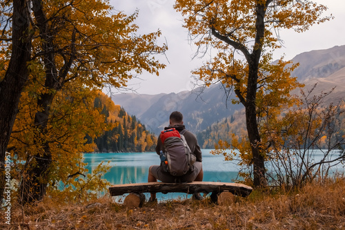 Tourist is resting on the bench near beautiful mountains lake with turquoise water and colorful forest. Tourism, trekking, hiking in autumn concept.