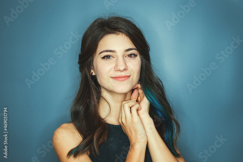 Smiling brunette with blue strands of hair, woman looking directly at the camera, lady with good looks, posing isolated on blue background, expressing happiness.