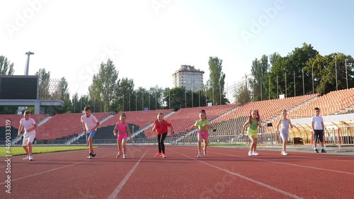 A group of children running on a treadmill at the stadium on a bright sunny day compete in who will be the fastest. Boys and a girl in colorful uniforms run a marathon at the stadium. Sport