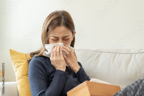 Sick, Coronavirus covid-19 asian young woman, girl headache under blanket have a fever, flu and use tissues paper sneezing nose, runny sitting on sofa bed at home. Health care on virus person.