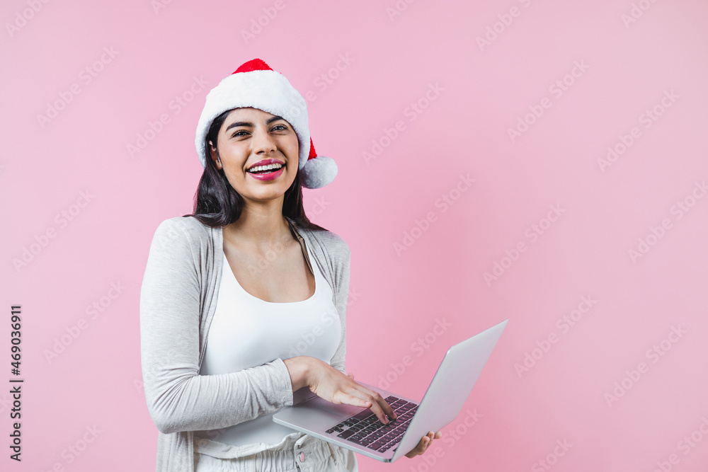Portrait of young latin woman holding a computer with copy space in a christmas concept on pink background Portrait of young latin woman holding a computer with copy space in a christmas concept on pink background