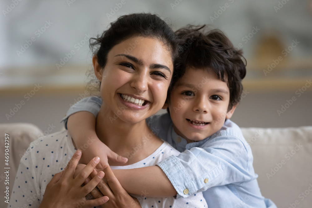Cheerful cute Indian preschooler kid embracing happy mother on couch