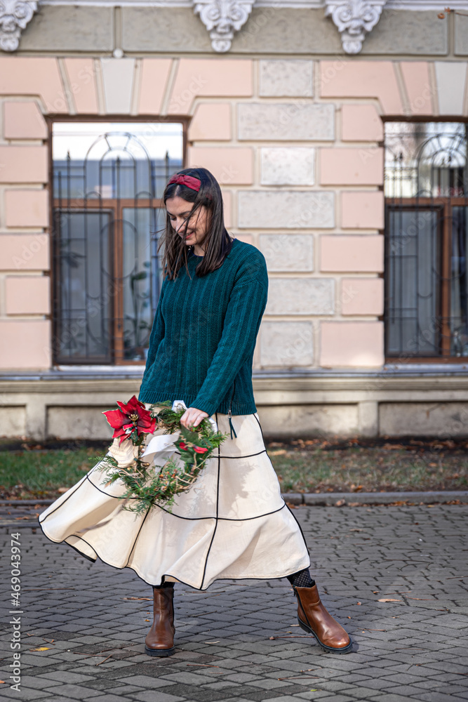 Stylish young woman with Christmas wreath outside, waiting for Christmas.