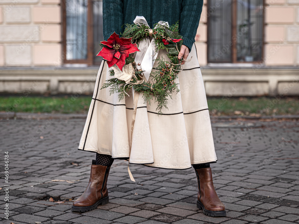 Christmas wreath in the hands of a stylish woman, city walk.