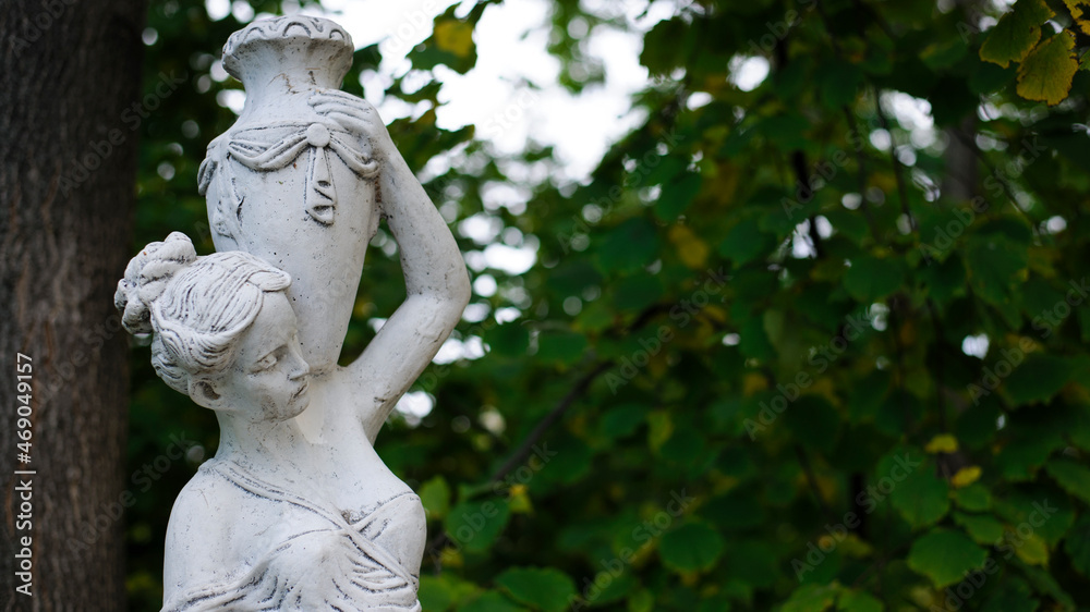 sculpture of a girl in the spring park. An old statue in a park of a sensual semi-nude Greek or Italian Renaissance woman with a vase in a city park. sunny day in the summer garden. close-up