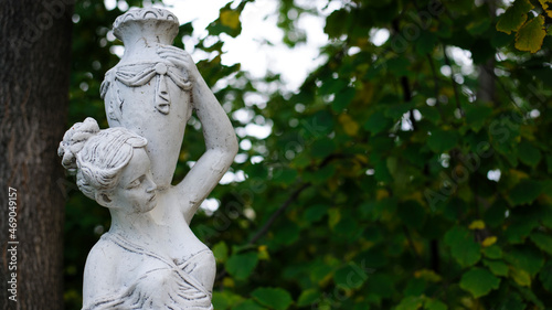 sculpture of a girl in the spring park. An old statue in a park of a sensual semi-nude Greek or Italian Renaissance woman with a vase in a city park. sunny day in the summer garden. close-up