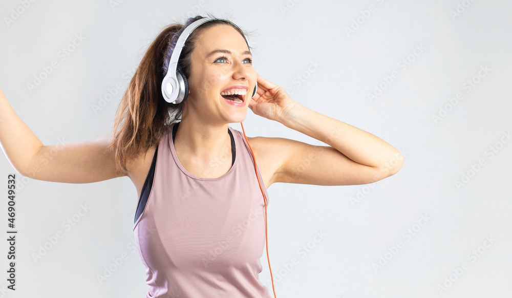 Sporty young woman in headphone holding smartphone and dancing over gray background. Sporty young woman in headphone holding smartphone and dancing over gray background.