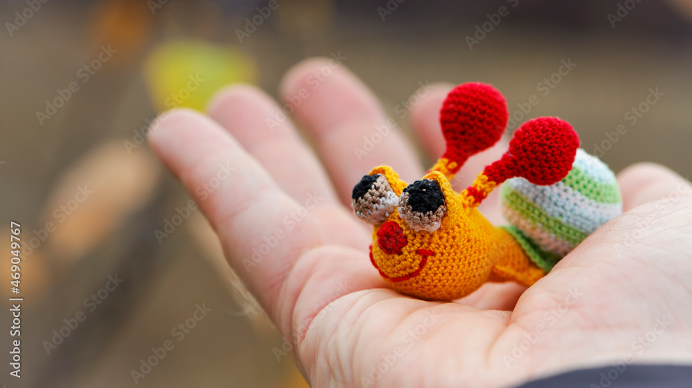 Textile handmade funny happy snail toy in hand on natural blurry background. macro photo. multi-colored snail. beautiful toy, close-up. the concept of childhood, games, education Textile handmade funny happy snail toy in hand on natural blurry background. macro photo. multi-colored snail. beautiful toy, close-up. the concept of childhood, games, education