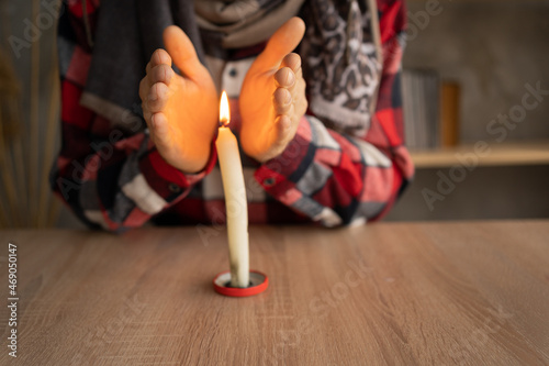 Close-up of male hands warming up near a burning candle which stands on the table. concept of problems with heating, cold at home in winter.