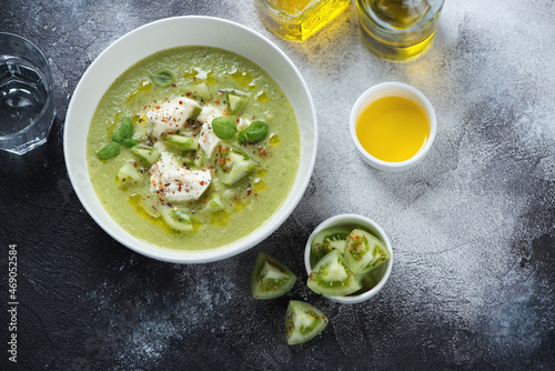 Bowl of green tomato gazpacho with mozzarella cheese, above view on a dark-grey stone background with space, horizontal shot