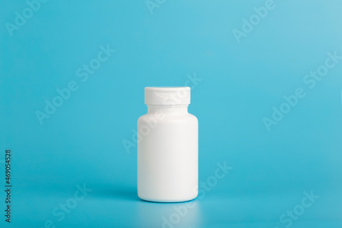 Jar of pills isolate. White plastic jar for medical pills, drugs and vitamins on a blank blue background.