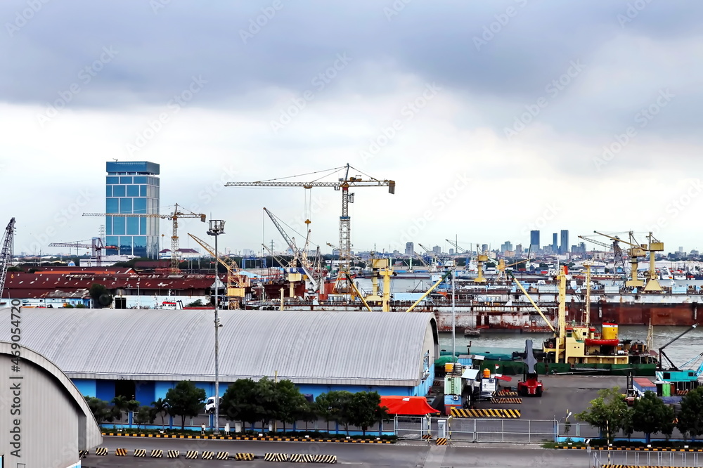 Fototapeta premium Cargo terminal for unloading steel plates from bulk carrier by ships cranes. View of the pier, cranes and various equipment. Port of Surabaya. Indonesia, January, 2021.