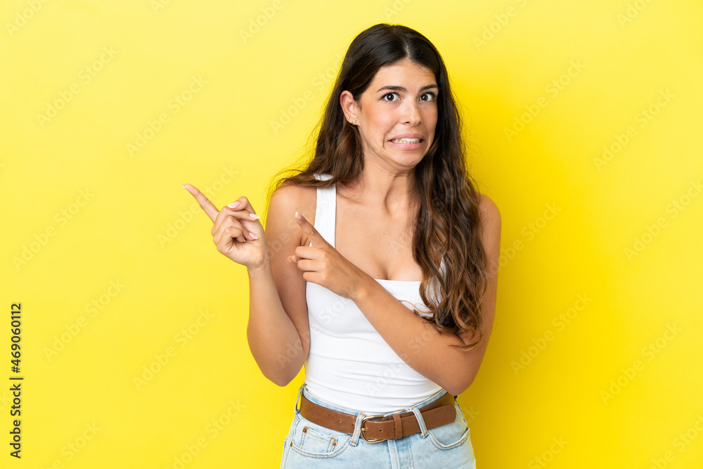 Young caucasian woman isolated on yellow background frightened and pointing to the side Young caucasian woman isolated on yellow background frightened and pointing to the side