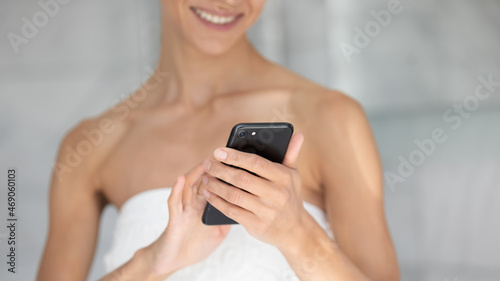 Close up cropped young mixed race woman wrapped in towel holding smartphone in hands, chatting in social network reading news after morning shower, checking period making notes in app, tech addiction.