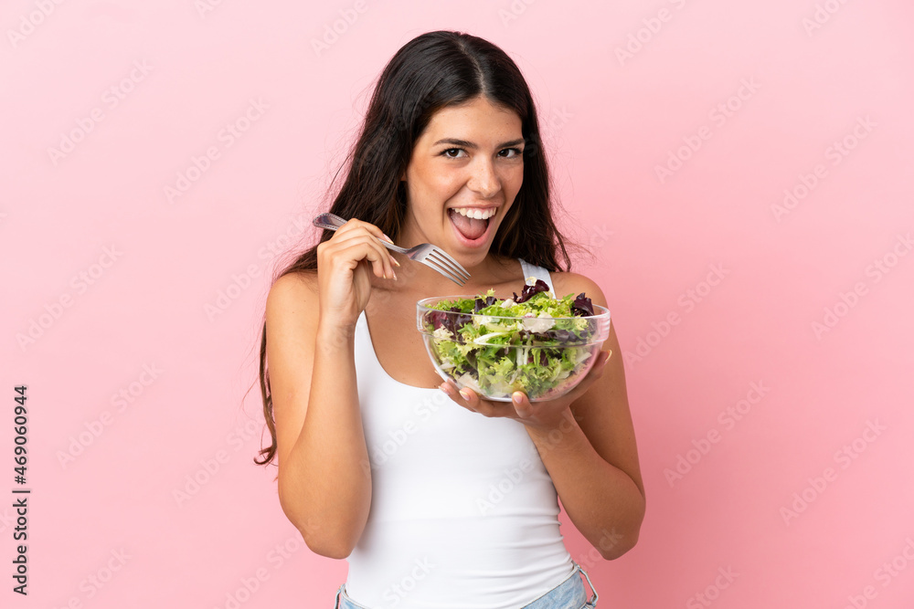 Young caucasian woman isolated on pink background holding a bowl of salad with happy expression