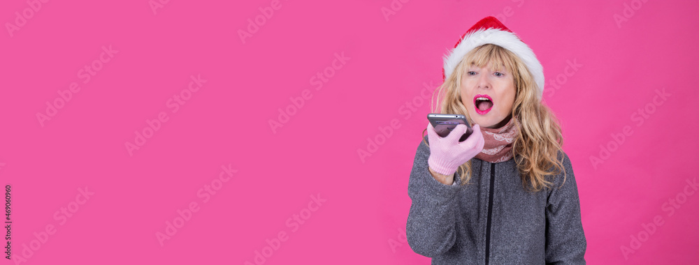happy excited woman in red santa claus hat with mobile phone isolated on pink background happy excited woman in red santa claus hat with mobile phone isolated on pink background