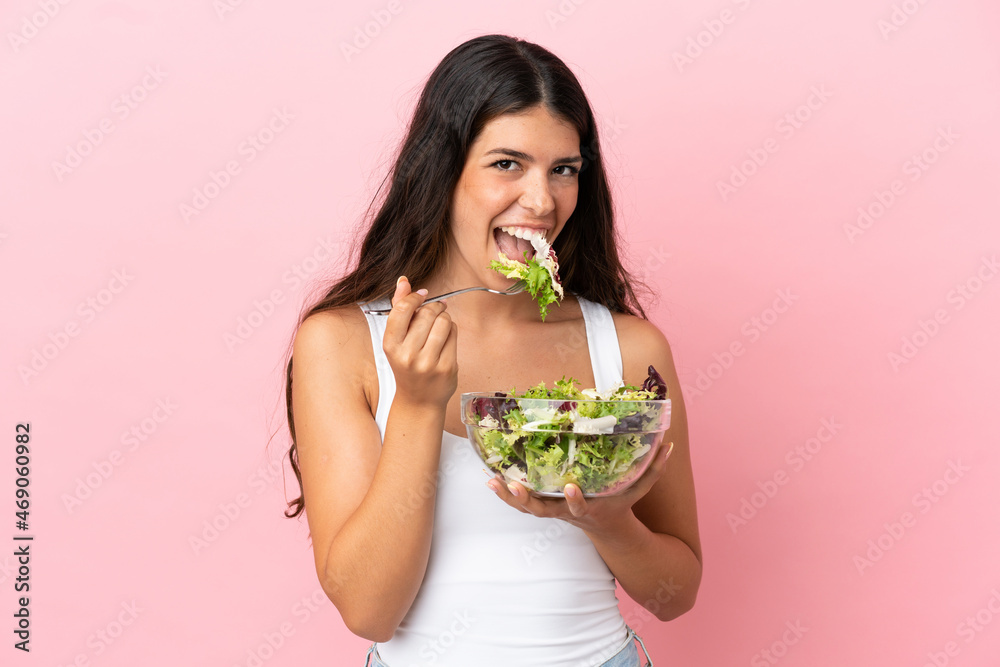 Young caucasian woman isolated on pink background holding a bowl of salad with happy expression