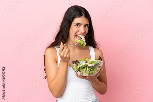 Young caucasian woman isolated on pink background holding a bowl of salad with happy expression