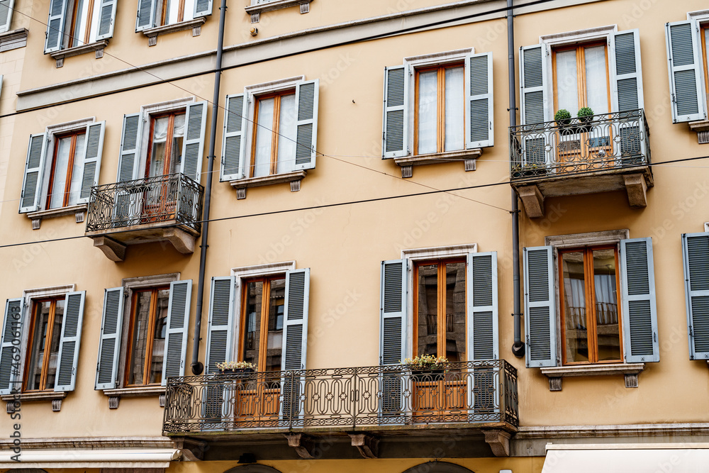 Facade of the building with shutters and wrought-iron balconies. Milan, Italy
