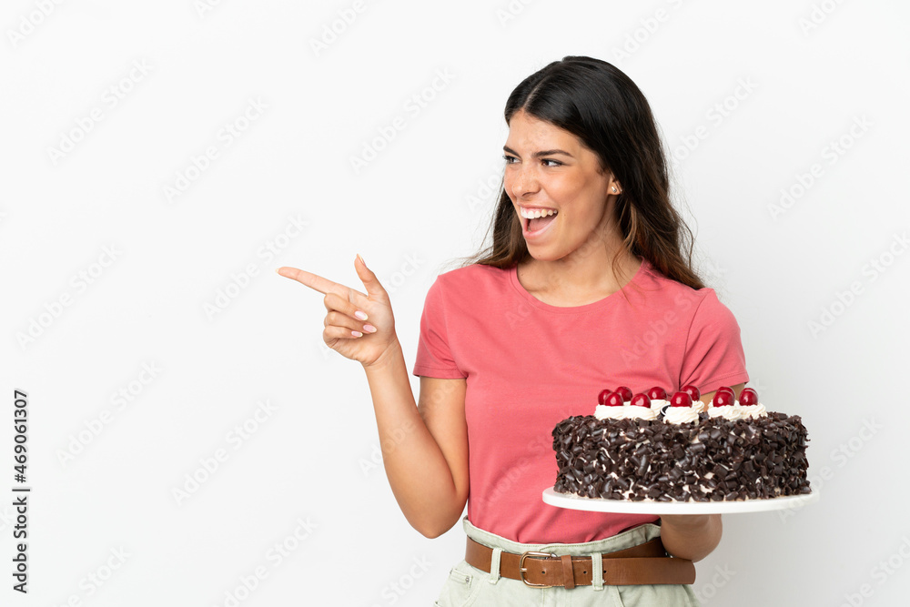 Young caucasian woman holding birthday cake isolated on white background pointing finger to the side and presenting a product Young caucasian woman holding birthday cake isolated on white background pointing finger to the side and presenting a product