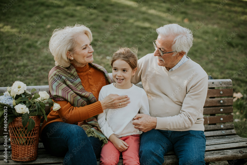 Senior couple sitting on the bench with their cute little granddaughter