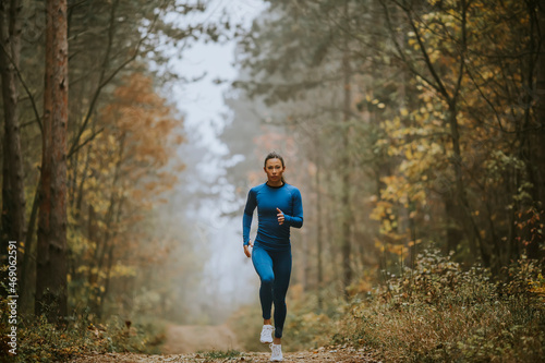 Young woman running toward camera on the forest trail at autumn