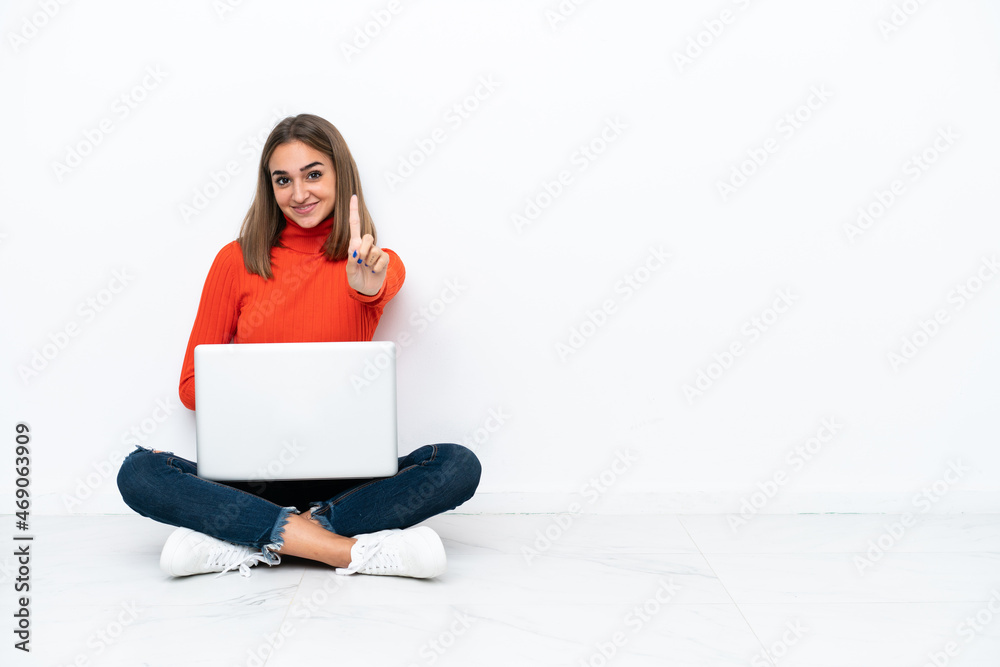 Young caucasian woman sitting on the floor with a laptop showing and lifting a finger Young caucasian woman sitting on the floor with a laptop showing and lifting a finger