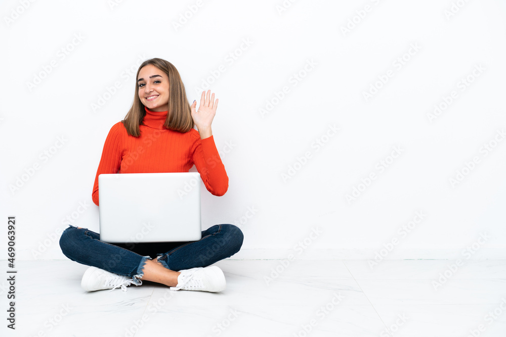 Young caucasian woman sitting on the floor with a laptop saluting with hand with happy expression Young caucasian woman sitting on the floor with a laptop saluting with hand with happy expression