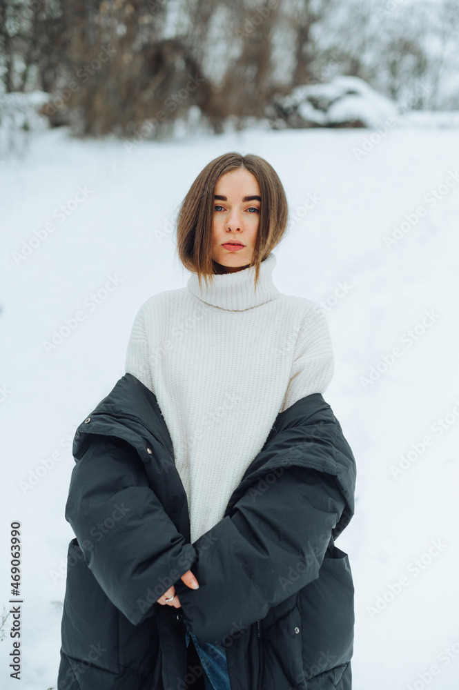 Attractive girl in a sweater stands on a snowy street in the cold and poses for the camera with a serious face with his jacket down. Attractive girl in a sweater stands on a snowy street in the cold and poses for the camera with a serious face with his jacket down.