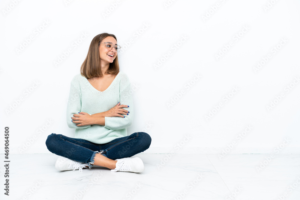 Young caucasian woman sitting on the floor isolated on white background happy and smiling