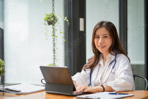 Young Asia lady doctor in white medical uniform with stethoscope using computer laptop