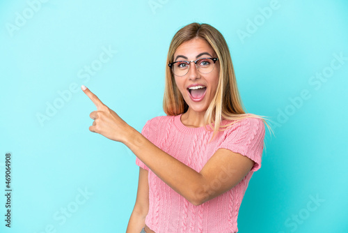 Blonde Uruguayan girl isolated on blue background surprised and pointing side