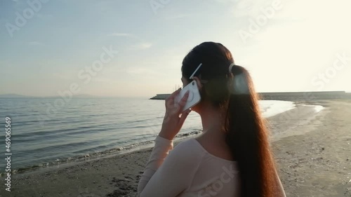 Happy young woman making a mobile phone call on the beach and smiling.
