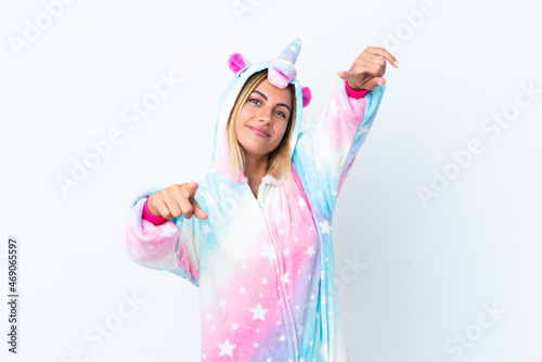 Blonde Uruguayan girl wearing a unicorn pajama isolated on white background points finger at you while smiling