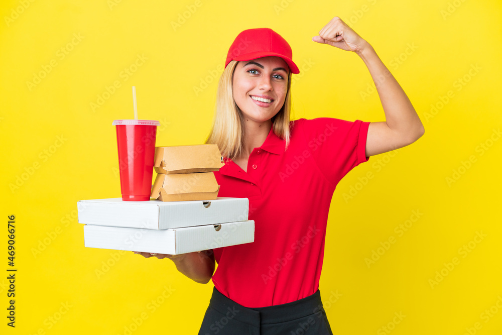 Delivery Uruguayan woman holding fast food isolated on yellow background doing strong gesture Delivery Uruguayan woman holding fast food isolated on yellow background doing strong gesture