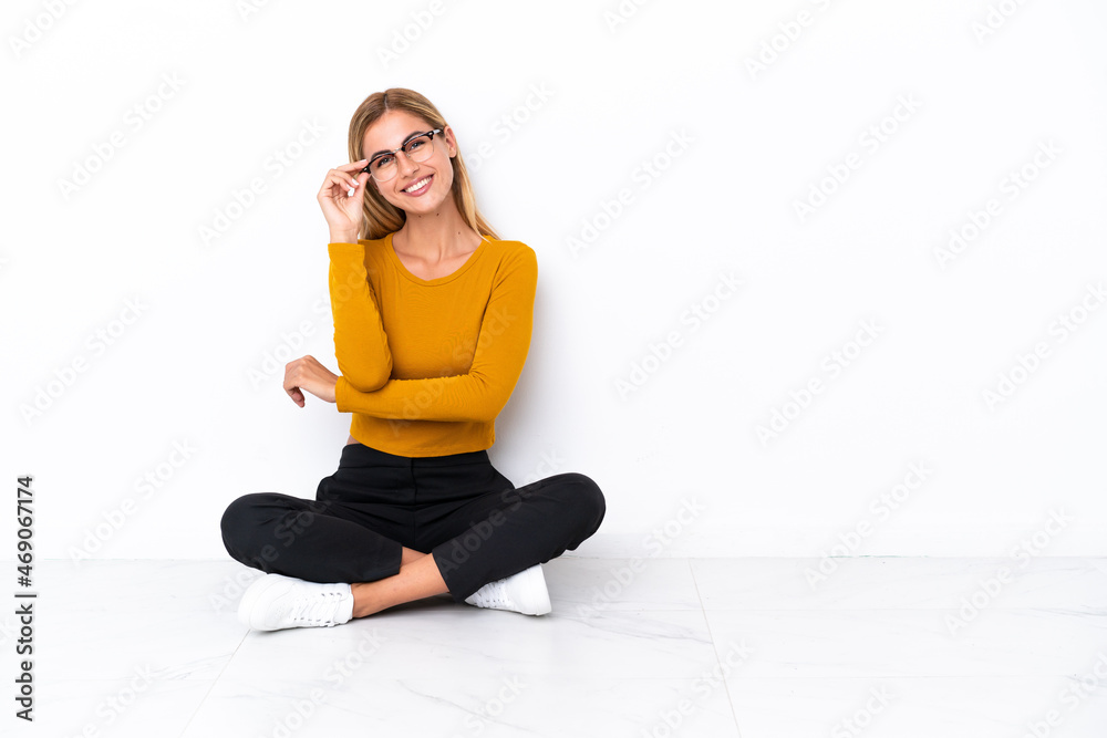 Blonde Uruguayan girl sitting on the floor with glasses and happy