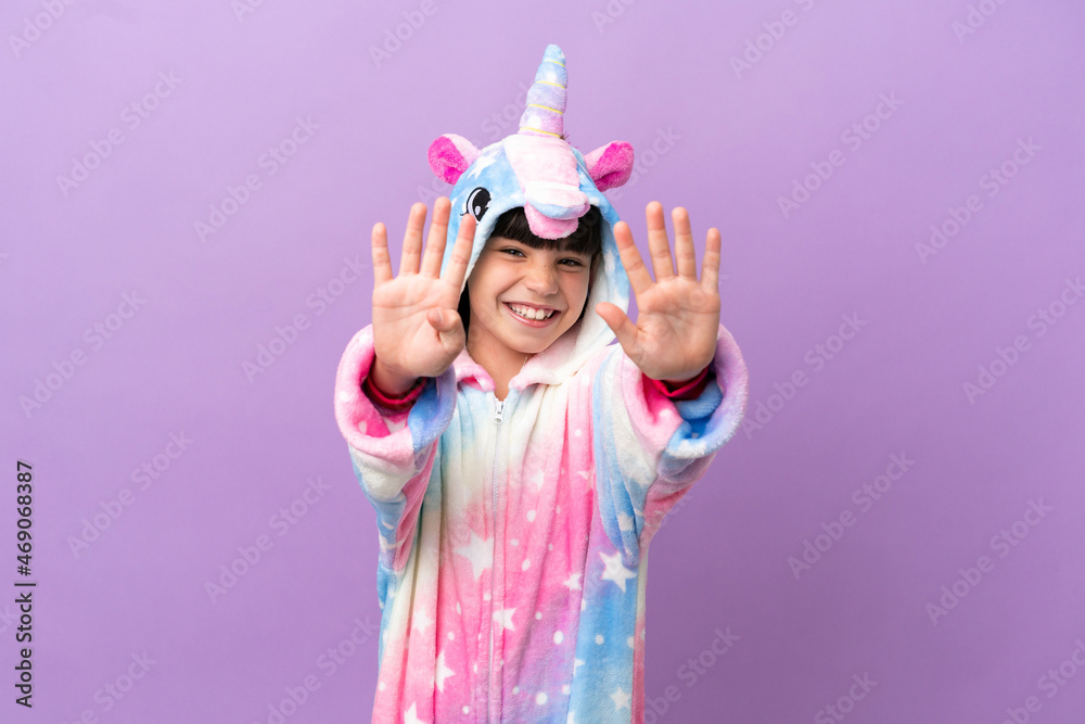 Little kid wearing a unicorn pajama isolated on purple background counting nine with fingers Little kid wearing a unicorn pajama isolated on purple background counting nine with fingers
