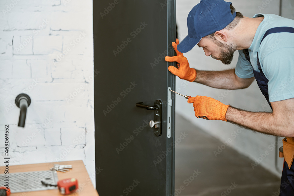 Bearded young man fixing door with screwdriver Bearded young man fixing door with screwdriver