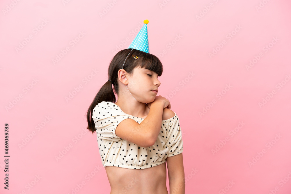 Little caucasian kid with birthday hat isolated on pink background suffering from pain in shoulder for having made an effort
