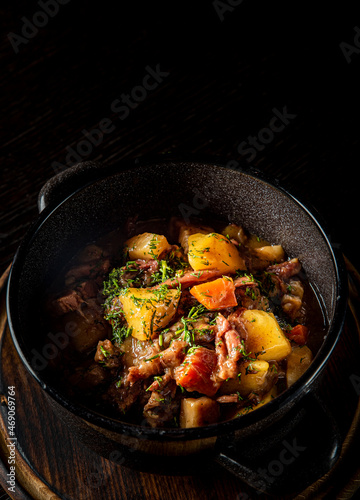 Goulash. Vegetable rague with meat, eggplant, pepper, potato and carrot in black bowl on dark wooden background