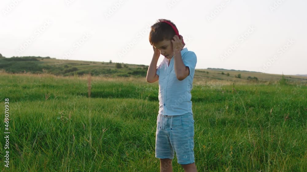 Charismatic six years old boy take his headphones and start running through the green field in the middle of nature and enjoy the moment and childhood Charismatic six years old boy take his headphones and start running through the green field in the middle of nature and enjoy the moment and childhood
